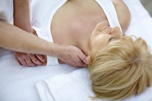 Doctor massaging a mature woman's neck in medical office